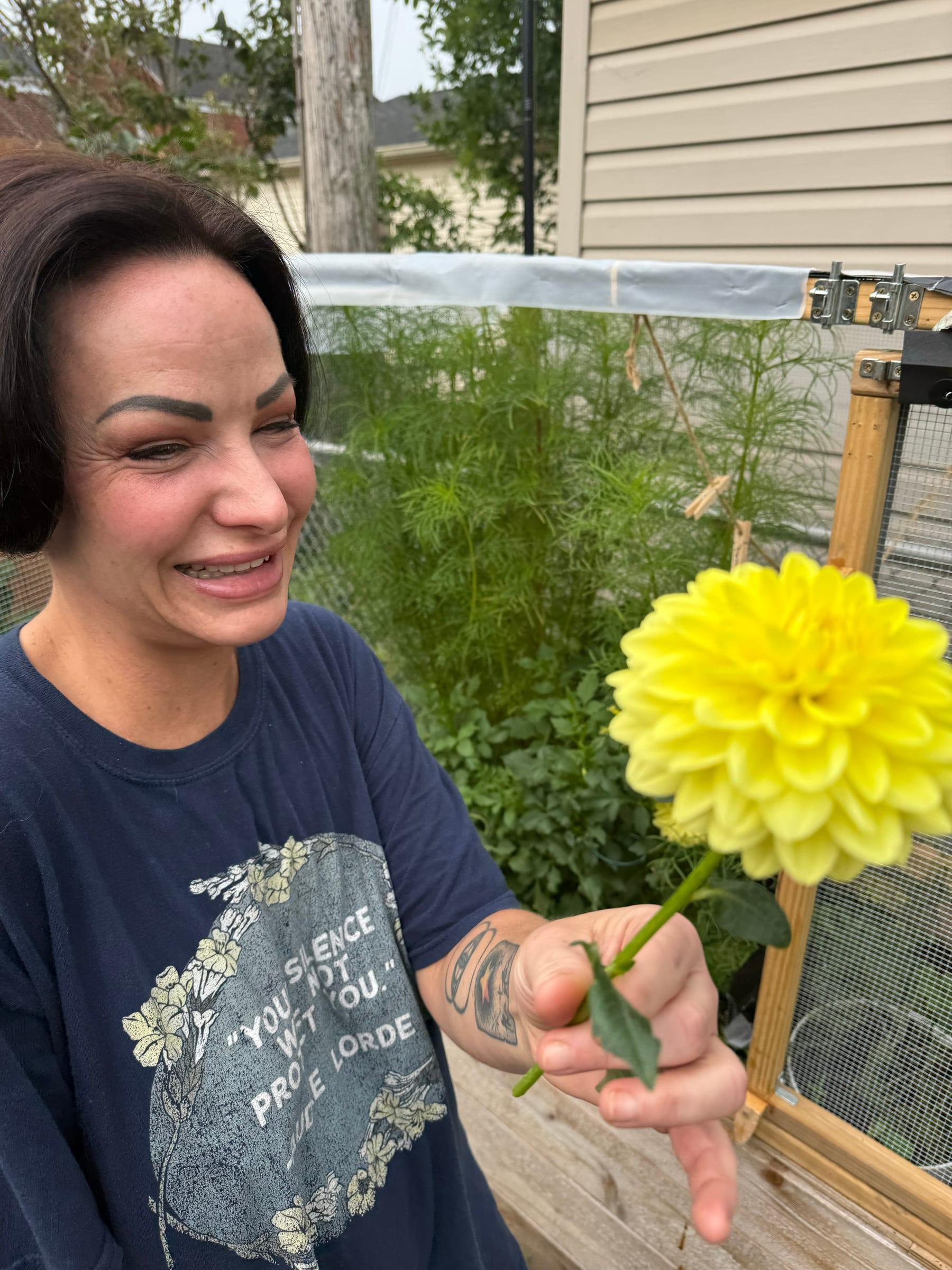 A smiling gardener holding up a bright yellow dahlia